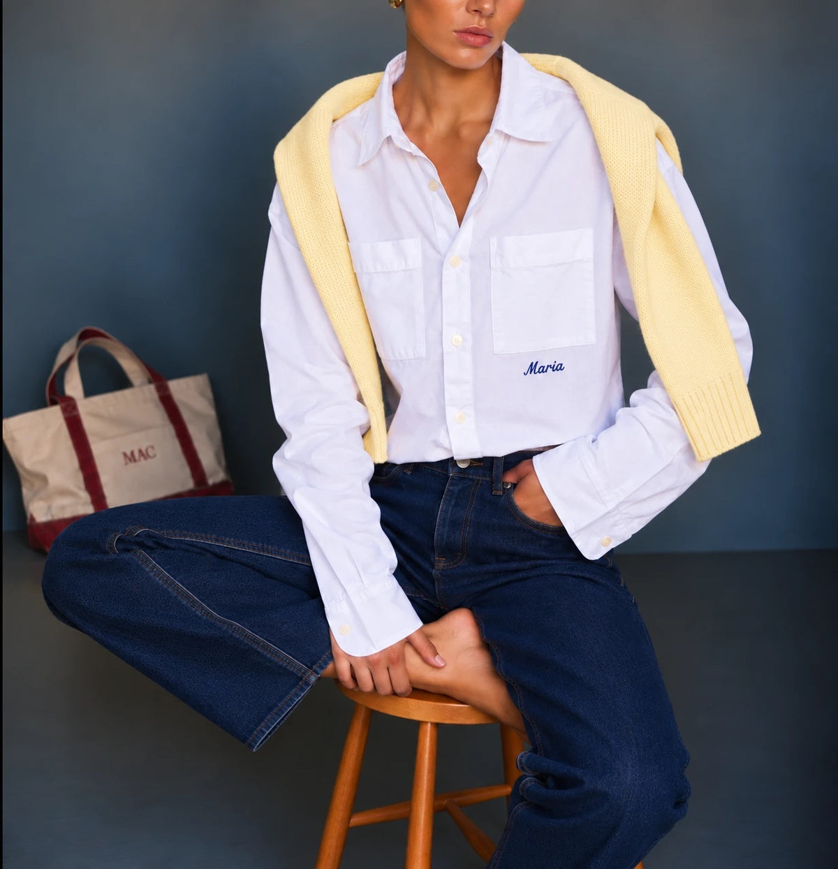 Mujer con camisa blanca bordada con el nombre Maria, un suéter amarillo en los hombros y un tote con MAC bordado